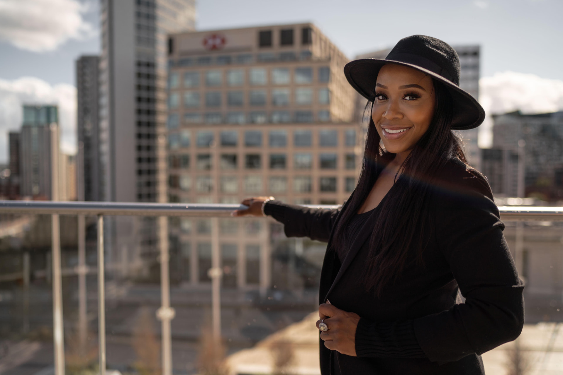 Elisha May in a black hat and blazer against a city skyline